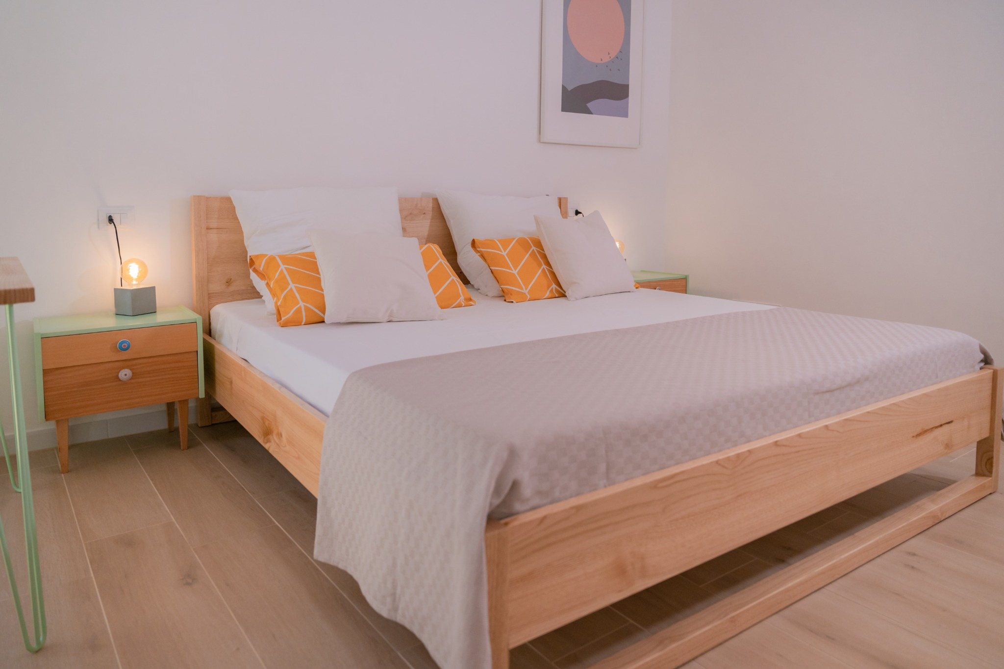 Helles Schlafzimmer mit großem Holzbett, weißen Kissen und warmen Akzentkissen.
