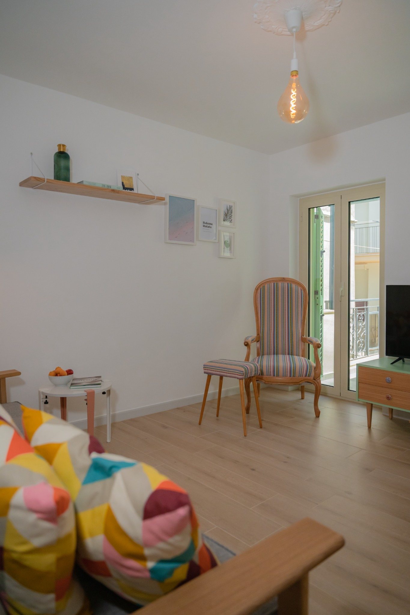 Wohnbereich mit Sofa, bunten Kissen, Sessel und Fenstertür.