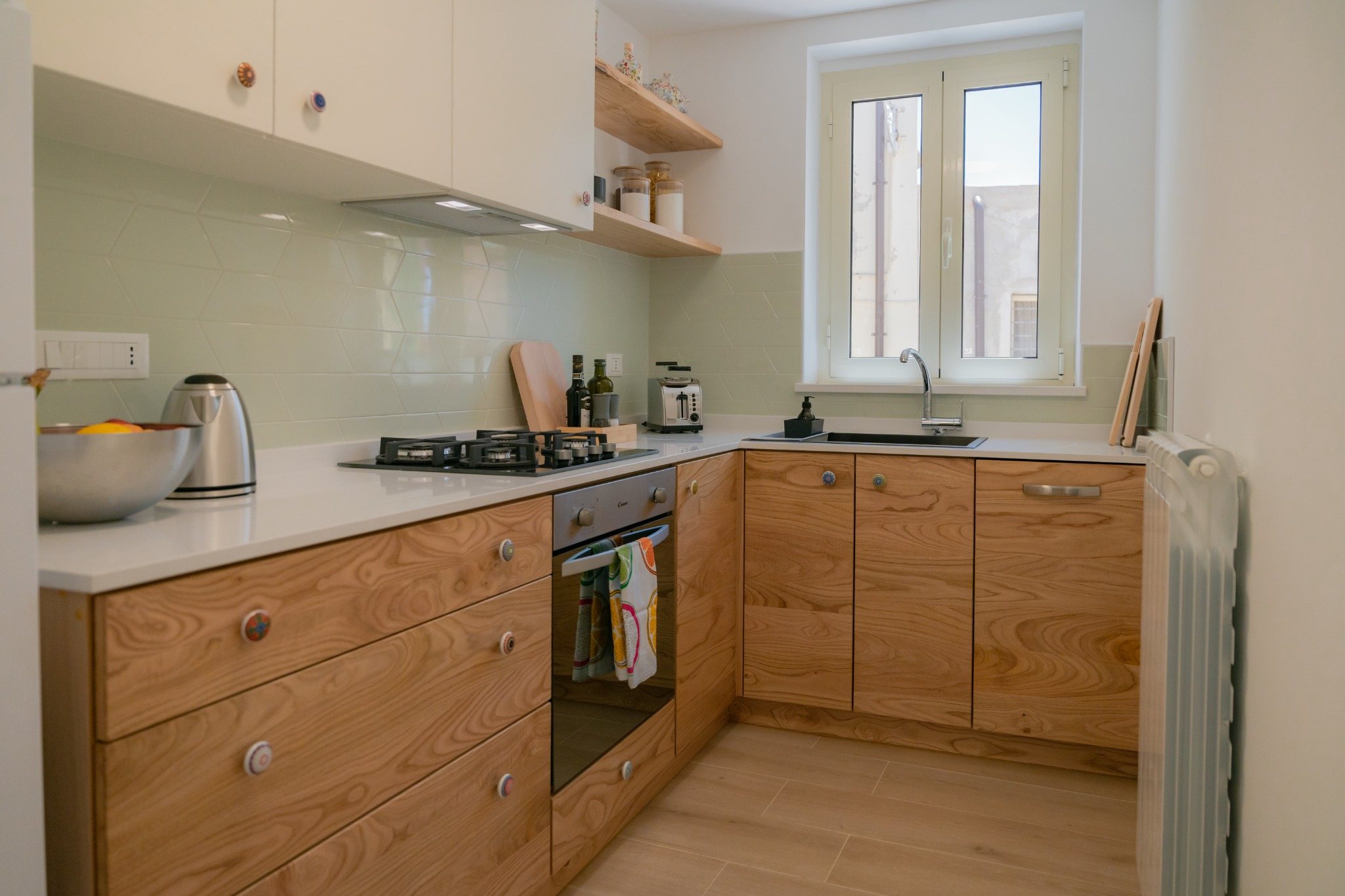 Helle Küche mit Holzfronten, Gasherd, Spüle und Fenster.