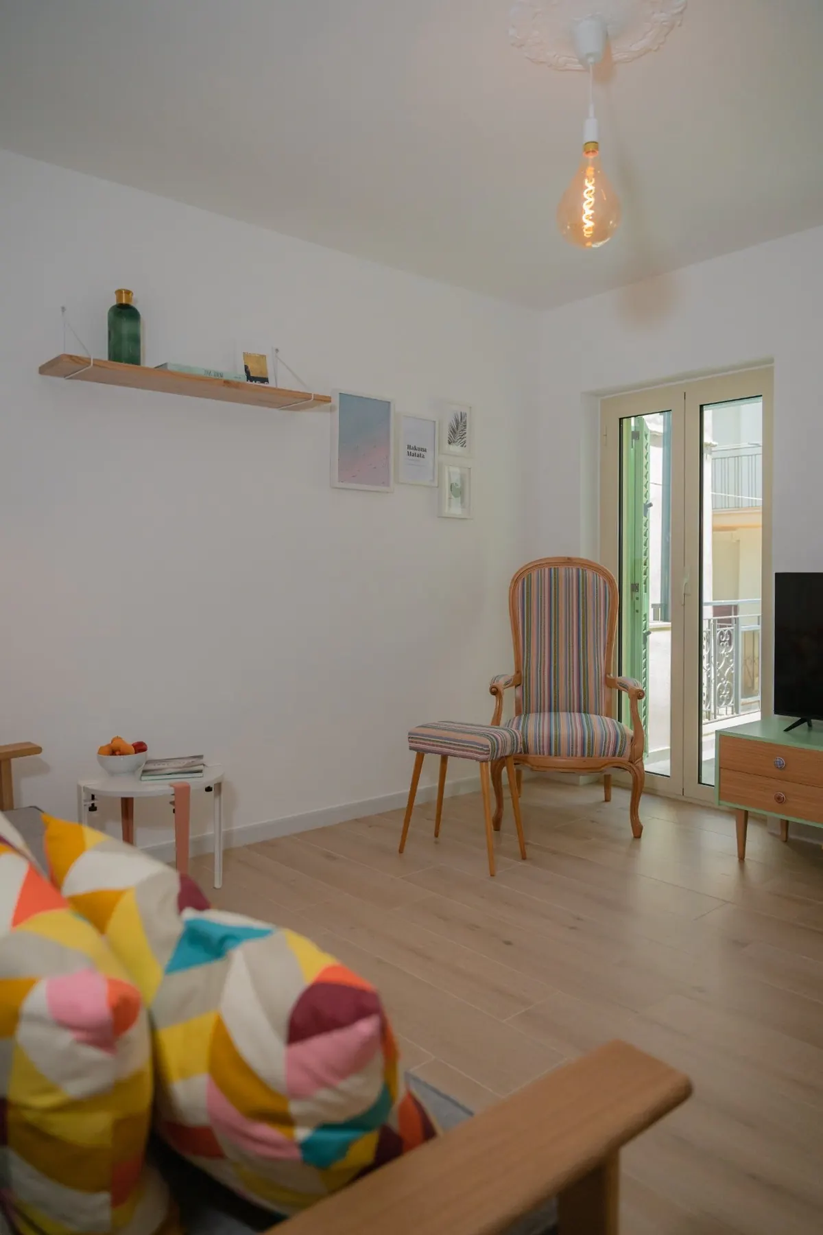 Wohnbereich mit Sofa, bunten Kissen, Sessel und Fenstertür.
