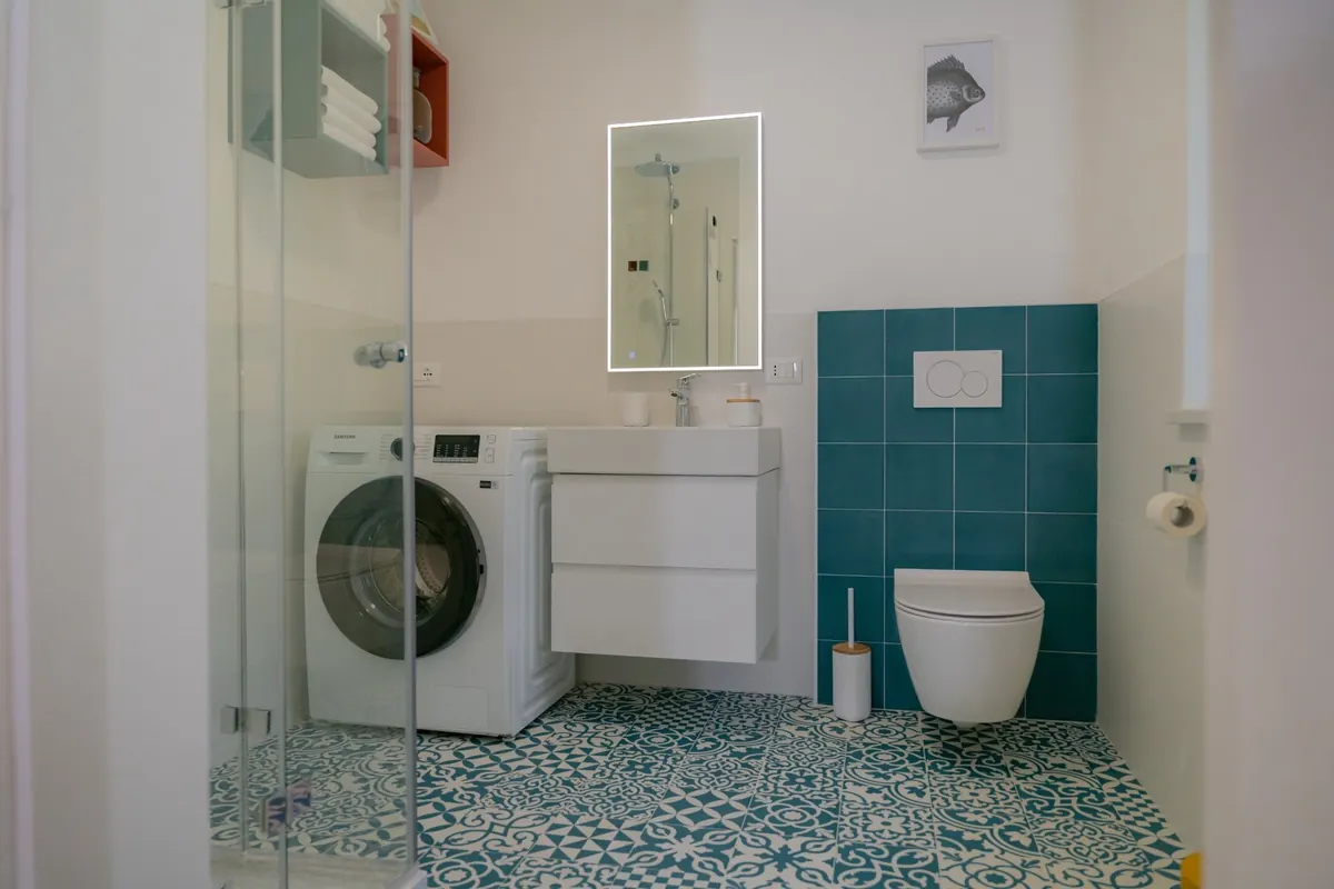 Modernes Bad mit Dusche, Waschbecken, Waschmaschine, WC und türkisfarbenen Fliesen.
